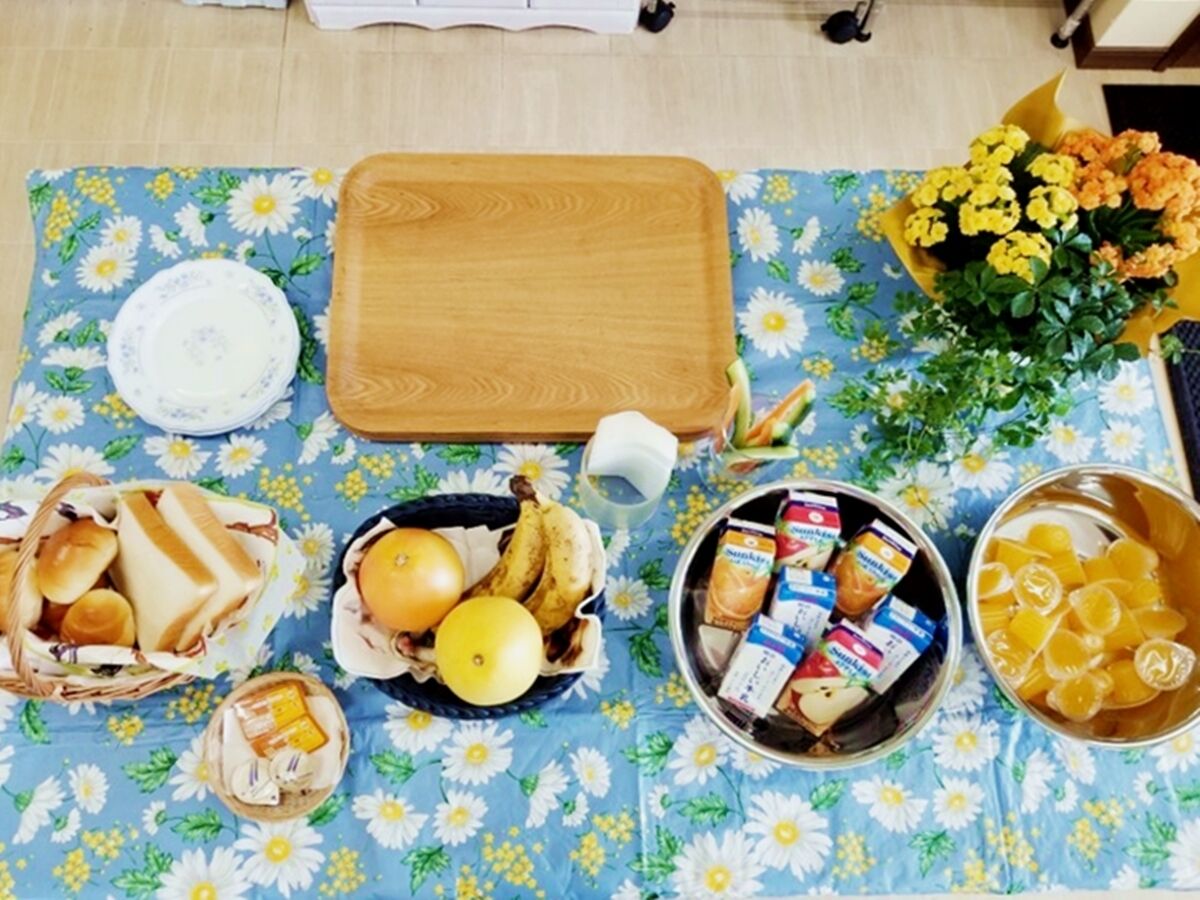 A table set with various food items, including bread, fruits, and condiments, on a floral tablecloth.