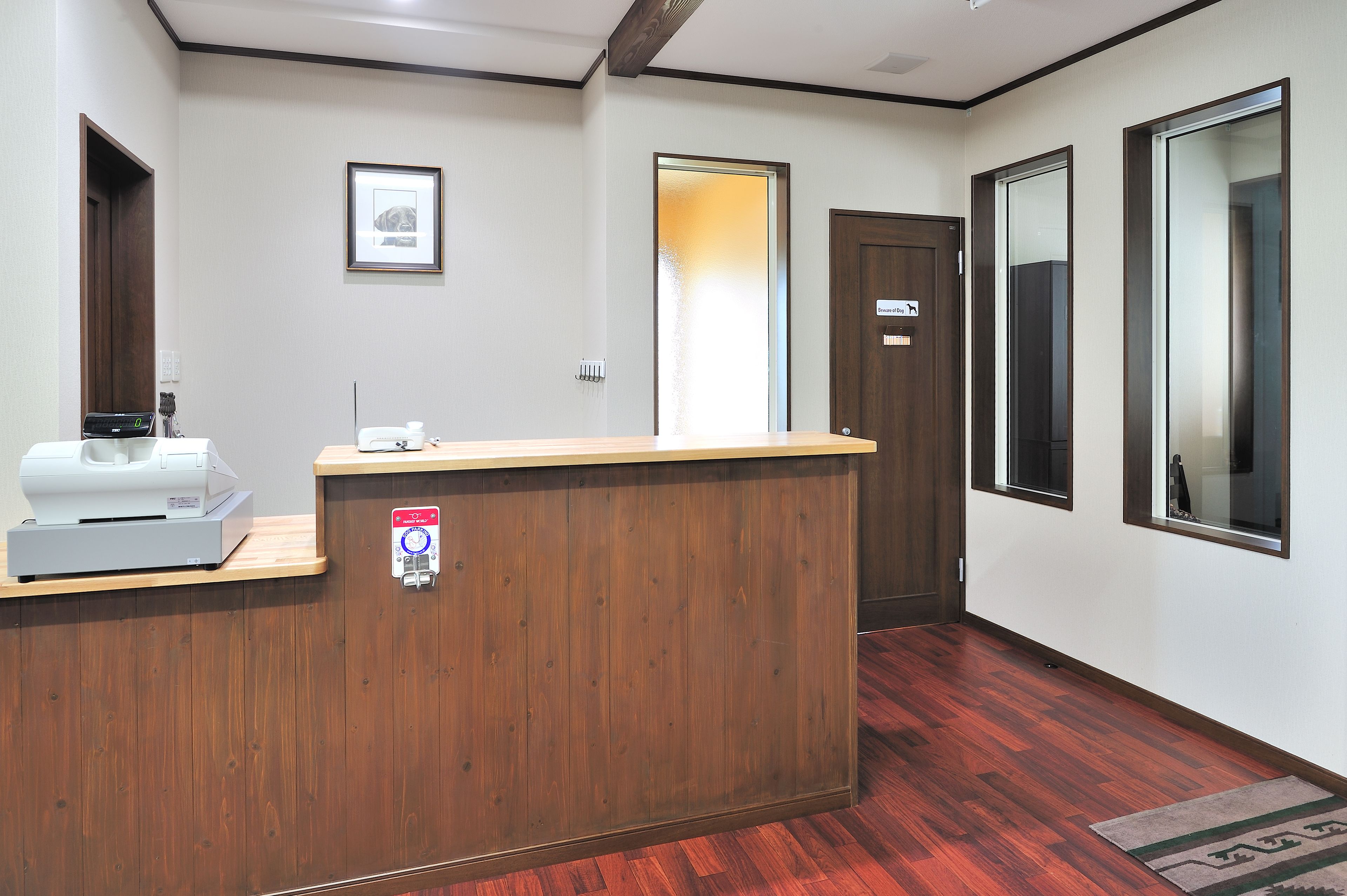 Uma área de recepção com um balcão de madeira, um quadro emoldurado na parede e uma porta com um aviso.