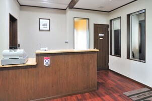 Uma área de recepção com um balcão de madeira, um quadro emoldurado na parede e uma porta com um aviso.