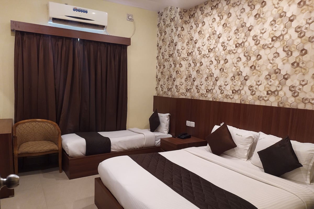 A hotel room with two beds, a chair, a nightstand, and a wall-mounted air conditioner.