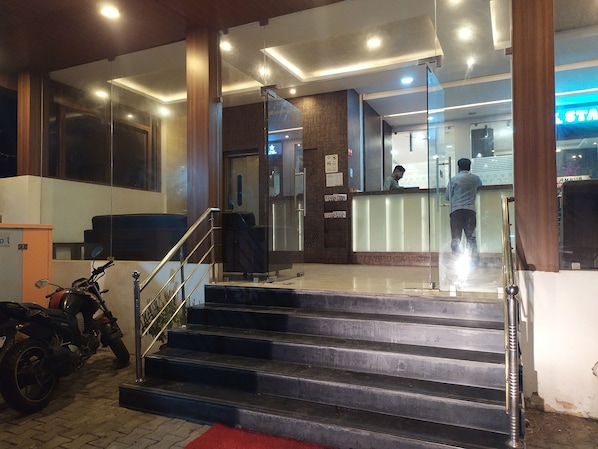 Un vestíbulo de hotel con una recepción, una escalera que sube al piso superior y una motocicleta estacionada.
