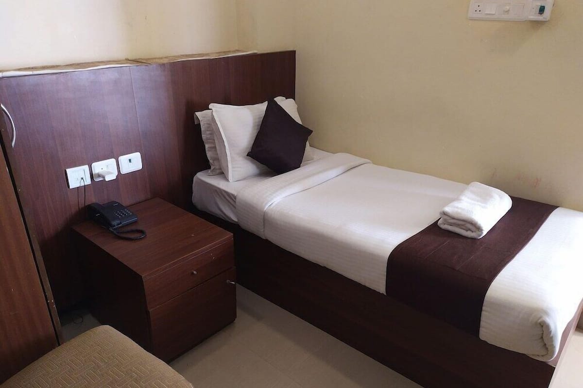 A single bed with a wooden headboard, a bedside table with a telephone, and a power outlet on the wall.