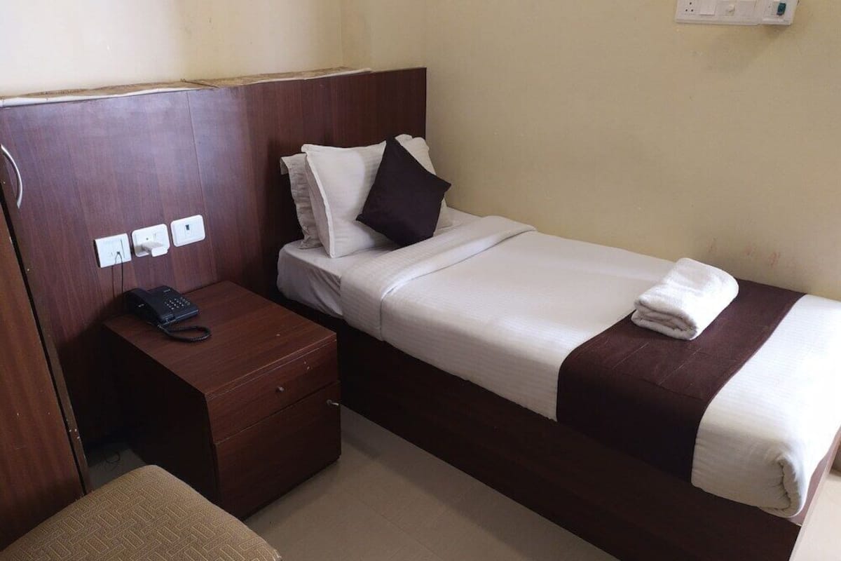 A single bed with a wooden headboard, a bedside table with a telephone, and a power outlet on the wall.