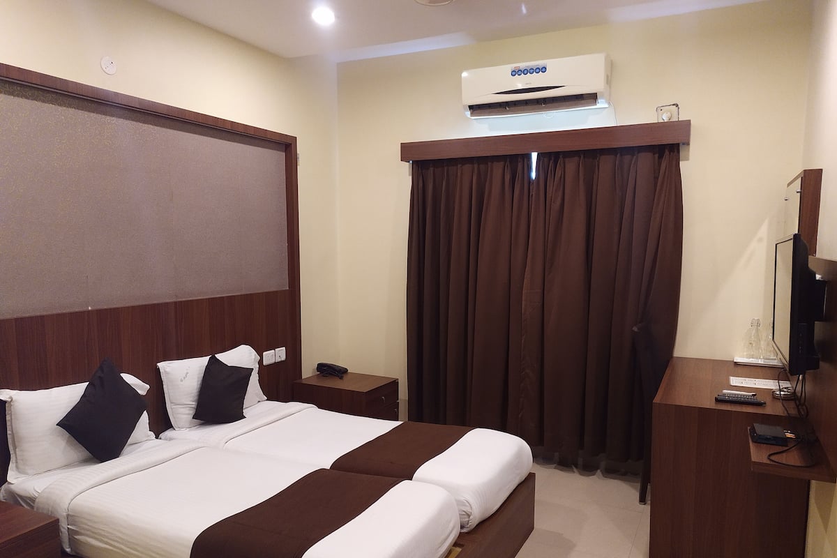A hotel room with a bed, a desk, a television, and an air conditioning unit.