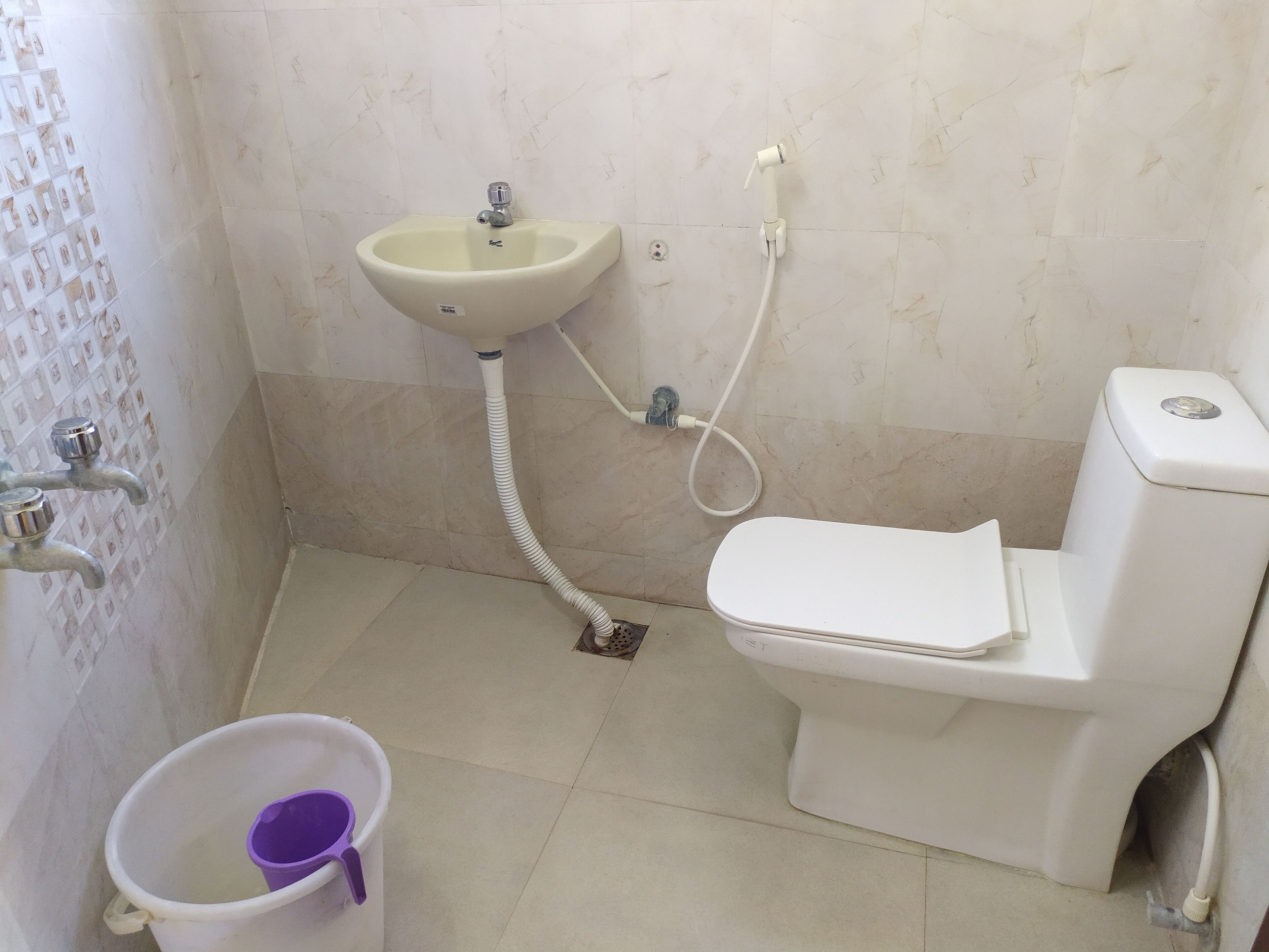 A bathroom with a toilet, a sink, and a bucket.