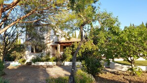 Una villa de estilo mediterráneo tradicional con un patio, rodeada de árboles maduros y un camino de grava.