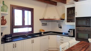 Una cocina con armarios blancos, encimera negra, mesa de madera y ventana con vistas.