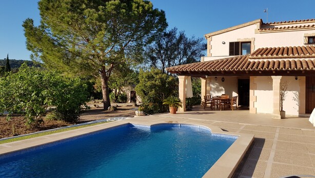Una piscina con solárium empedrado, un patio con mobiliario exterior y un edificio con tejado de tejas.