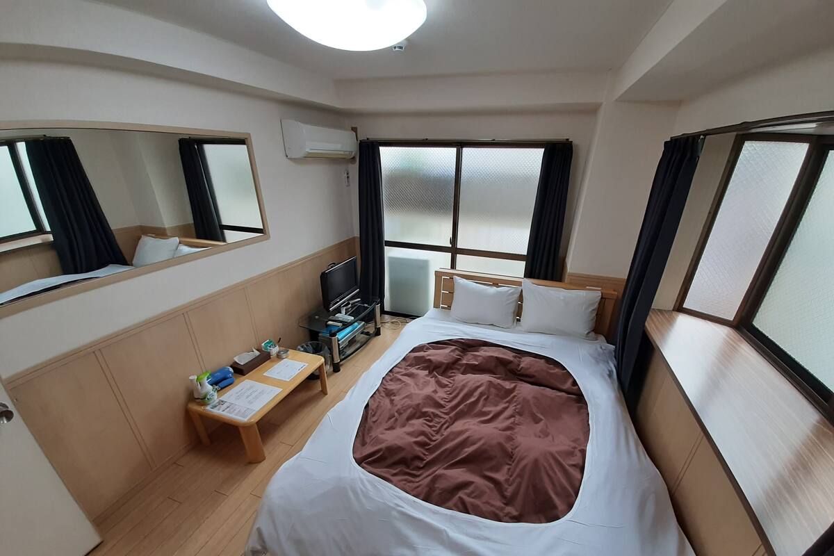 Habitación de hotel con cama, escritorio, televisión y ventana con cortinas.