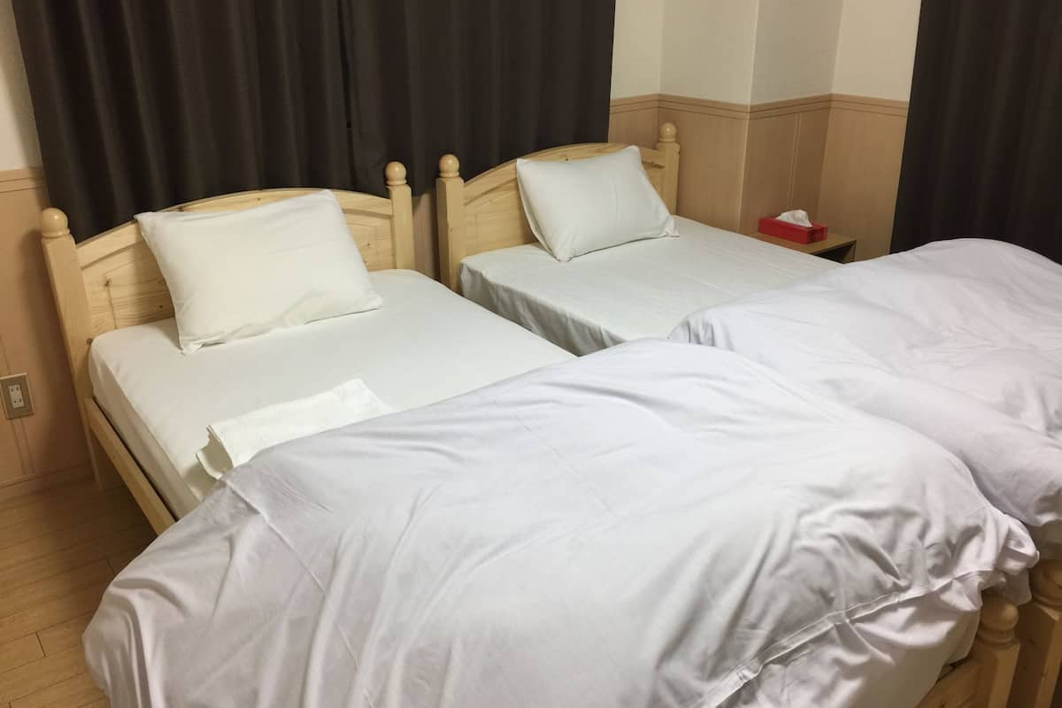 Dos camas individuales con cabeceros de madera y ropa de cama blanca en una habitación con cortinas oscuras y suelo de madera.