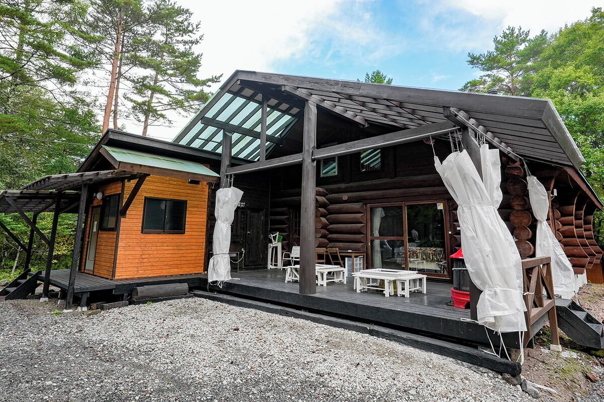 A log cabin with a covered patio, outdoor seating, and a glass-enclosed porch.