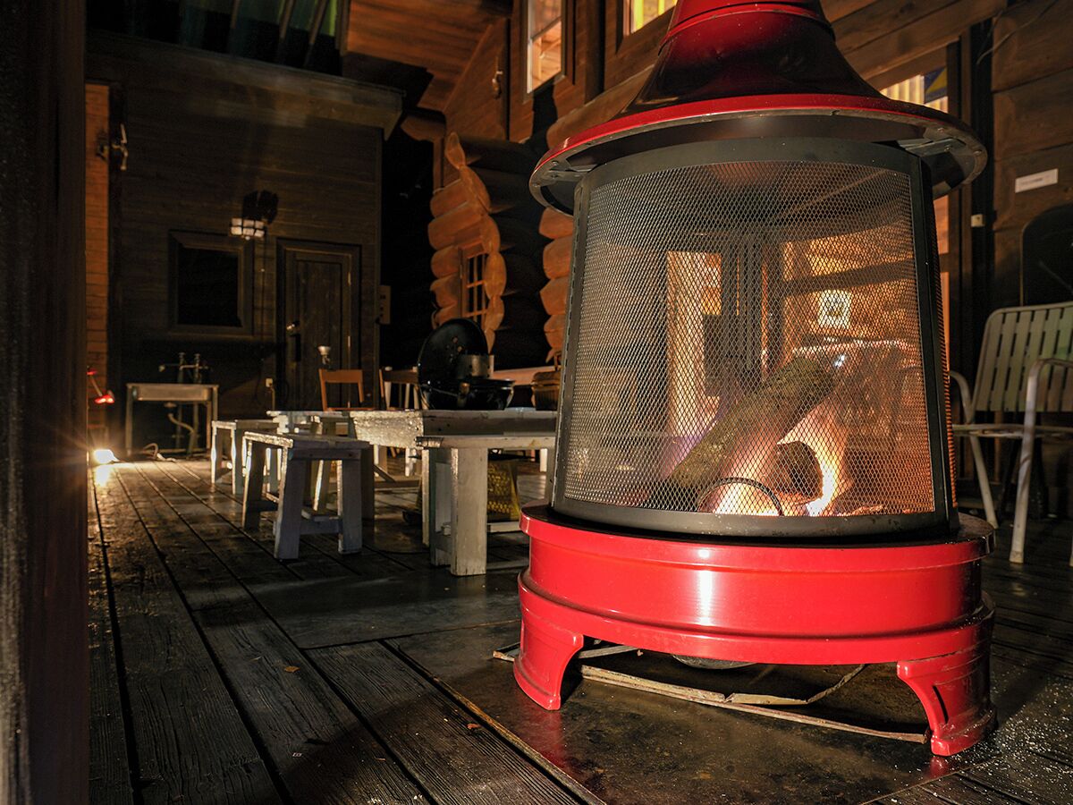 A red outdoor heater on a wooden deck with tables and chairs.