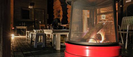 A red outdoor heater on a wooden deck with tables and chairs.