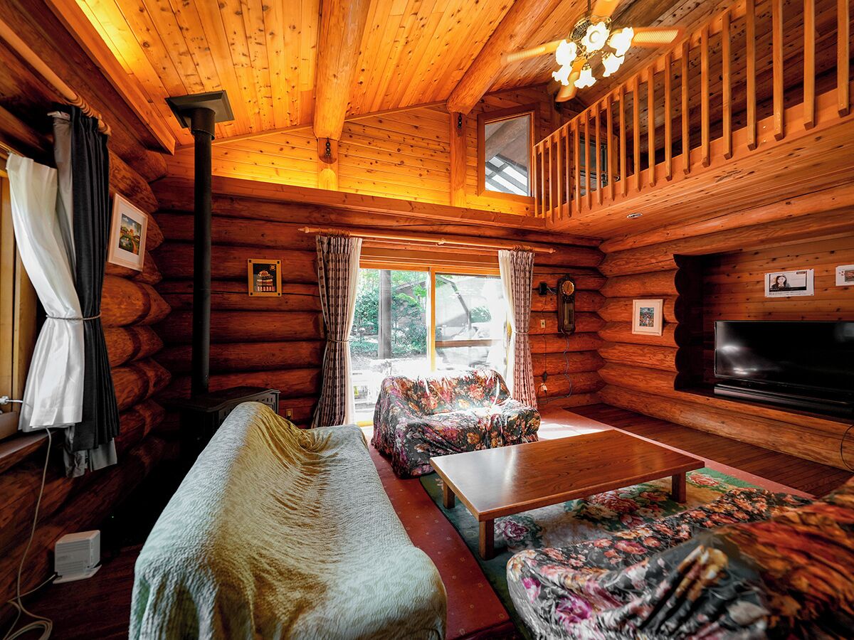 A cozy log cabin interior with a sofa, a television, and a dining table.