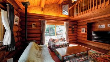 A cozy log cabin interior with a sofa, a television, and a dining table.