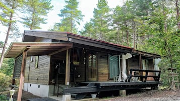 A rustic cabin with a porch, a covered deck, and a gravel driveway surrounded by trees.