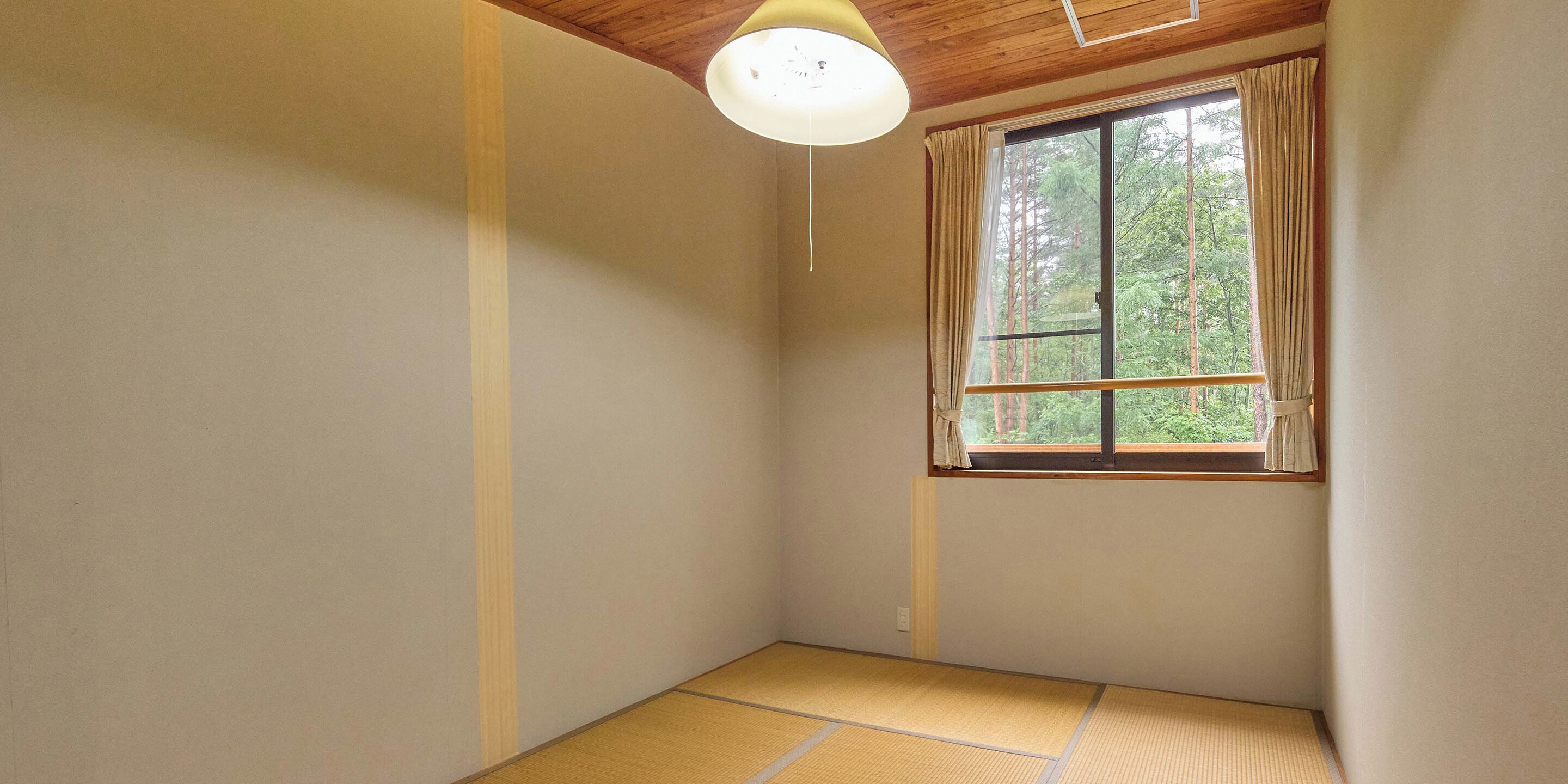 Una habitación con suelo de tatami, una ventana con cortinas y una lámpara en el techo.