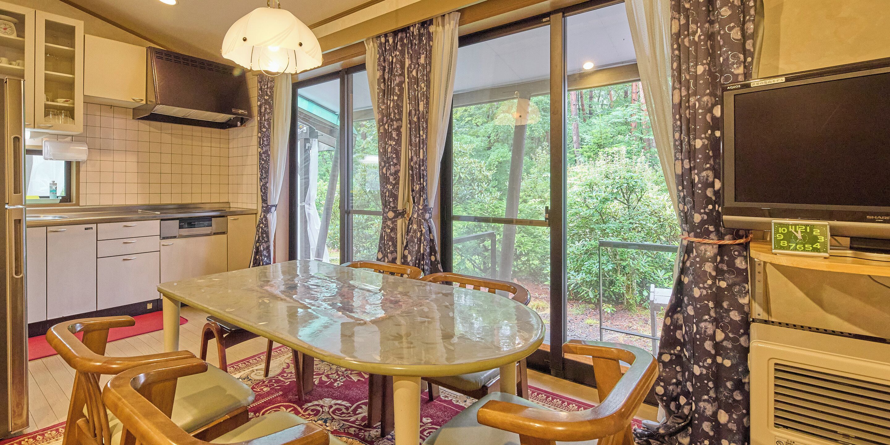 A modern kitchen with a dining area, large windows, and a flat-screen TV.