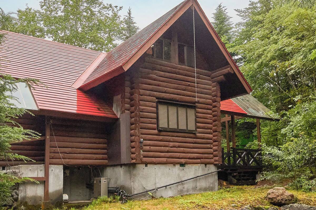 A log cabin with a steeply pitched roof, a small porch, and a window with shutters.