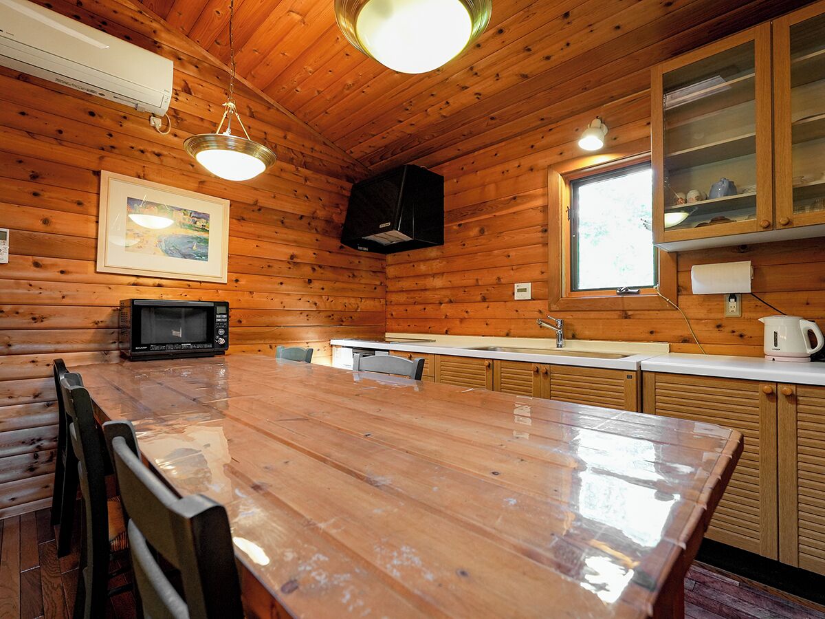 Ein Holzblock-Interieur mit Esstisch, Stühlen, einer Mikrowelle, einem Spülbecken und Schränken.