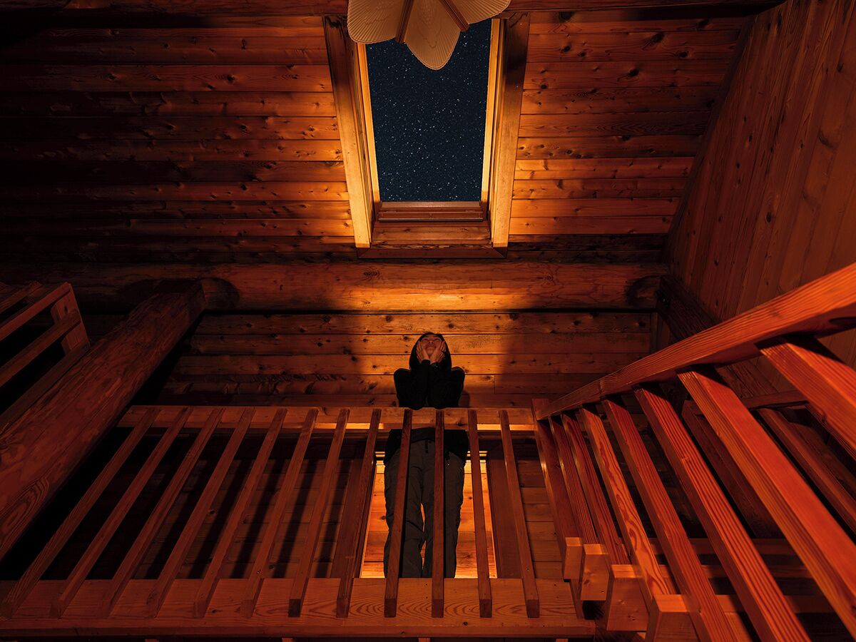 A wooden attic room with a sloped ceiling, a small window, and a wooden ladder.