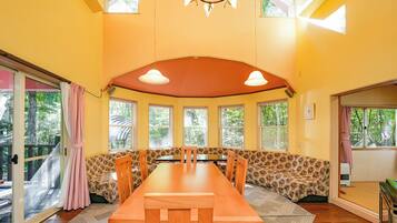 Uma sala de jantar com uma mesa de madeira comprida, assentos acolchoados e grandes janelas.