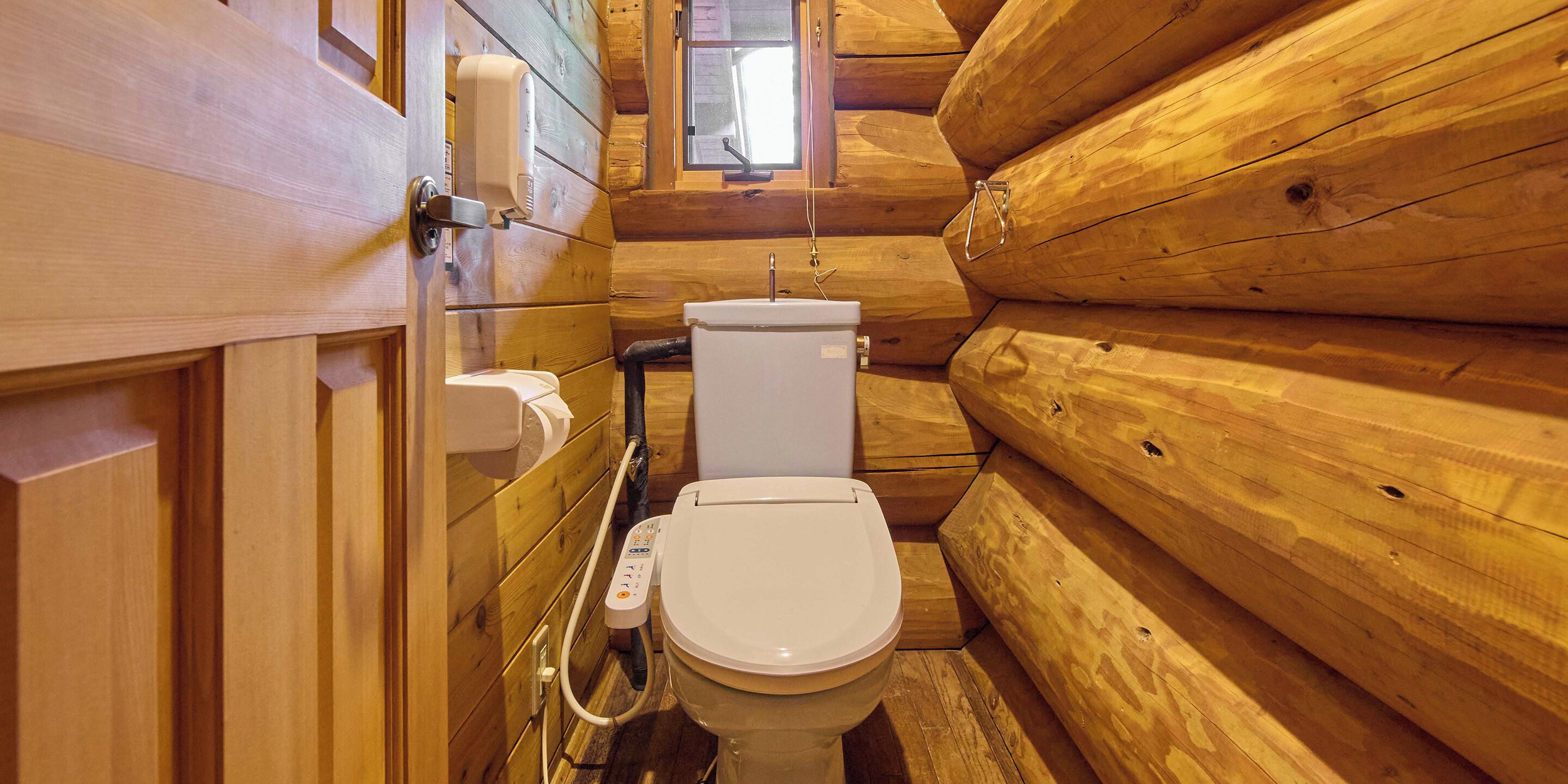 A wooden cabin-style bathroom with a toilet, a hand dryer, and a window.
