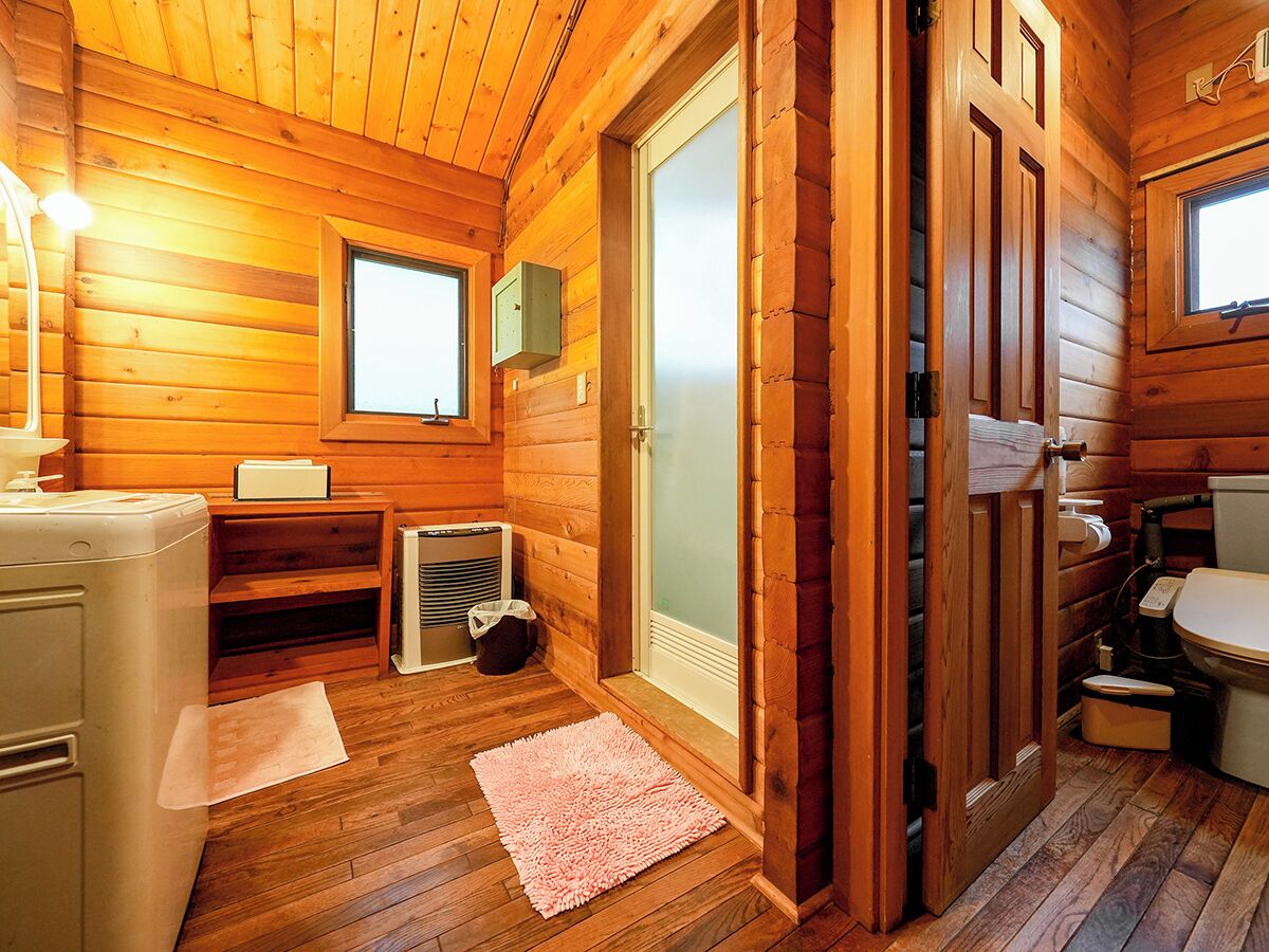 A wooden cabin bathroom with a toilet, sink, and a small window.