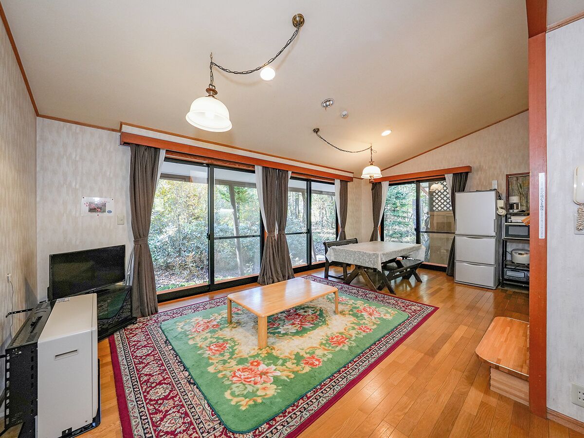 Amplia sala de estar con piso de madera, comedor con mesa y sillas, televisor y refrigerador.