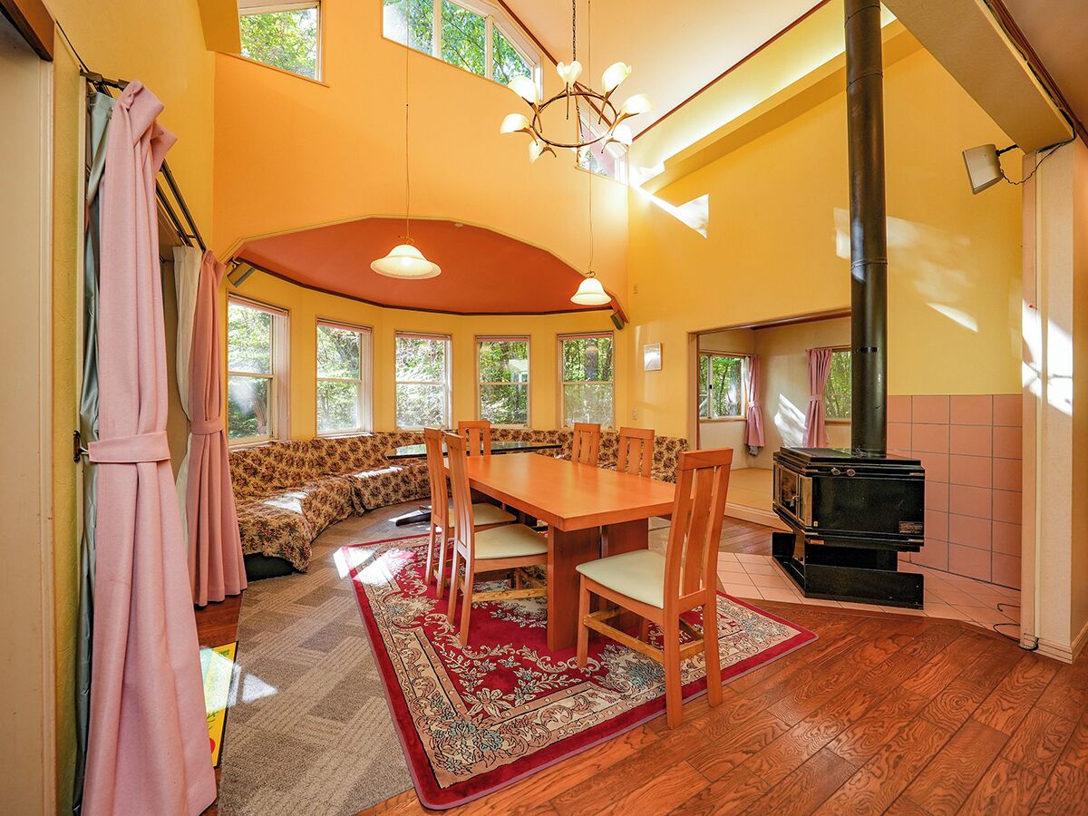 A cozy room with a wooden dining table, chairs, a sofa, and a large window.
