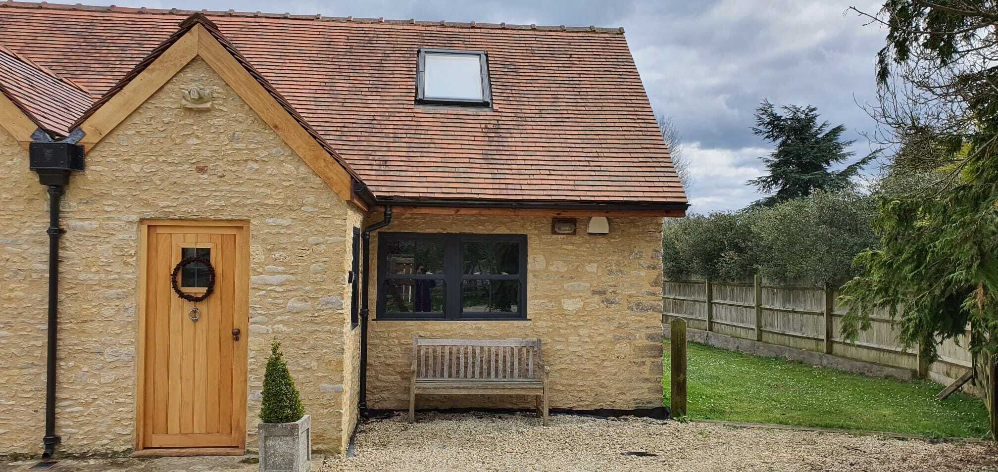Un bâtiment en pierre avec une porte en bois, une petite fenêtre et un banc à l’extérieur.