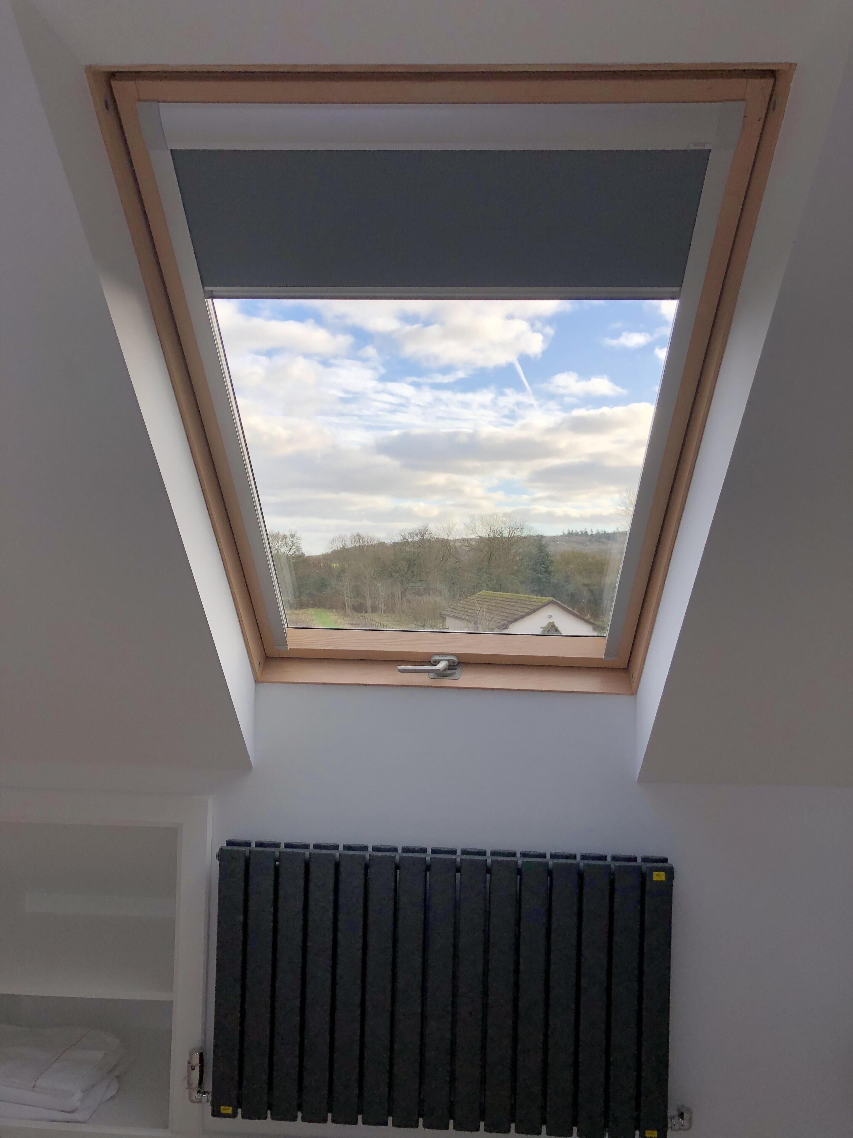 Een dakraam met uitzicht op een bewolkte lucht en verre gebouwen.