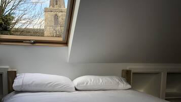 A bedroom with a bed, white bedding, a window with a view of a church spire, and a wooden headboard.
