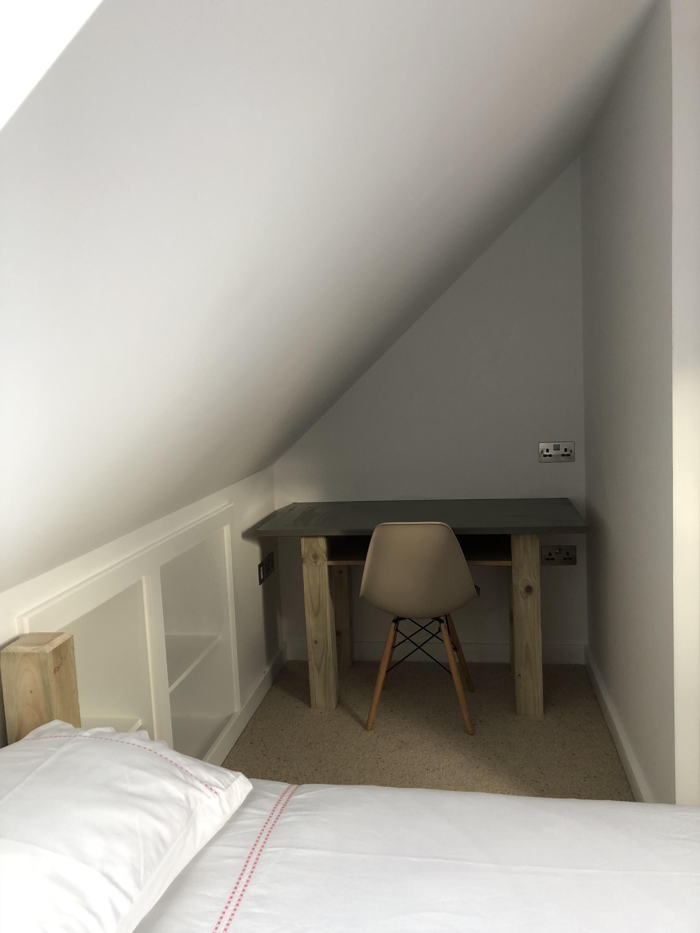A small, sloped ceiling room with a bed, a desk, and a chair.