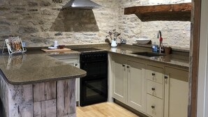 A kitchen with a central island, a built-in oven, a stone wall, and wooden beams. - Beautiful self contained Cotswold style cottage 15 mins Central Oxford (Cassington)