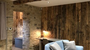 A room with exposed wooden beams, a stone wall, a blue sofa, and a granite countertop. - Beautiful self contained Cotswold style cottage 15 mins Central Oxford (Cassington)