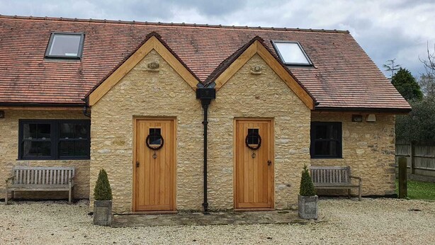 A stone building with two wooden doors, a gravel driveway, and a wooden bench. - Beautiful self contained Cotswold style cottage 15 mins Central Oxford (Cassington)