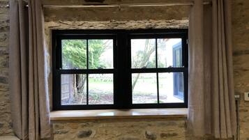 Ein Raum mit Steinwänden, einem großen Fenster, Vorhängen und einer Holzbalkendecke.