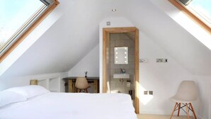 A bedroom with a sloped ceiling, a bed, a desk, a chair, a vanity with a mirror, and a small window. - Beautiful self contained Cotswold style cottage 15 mins Central Oxford (Cassington)