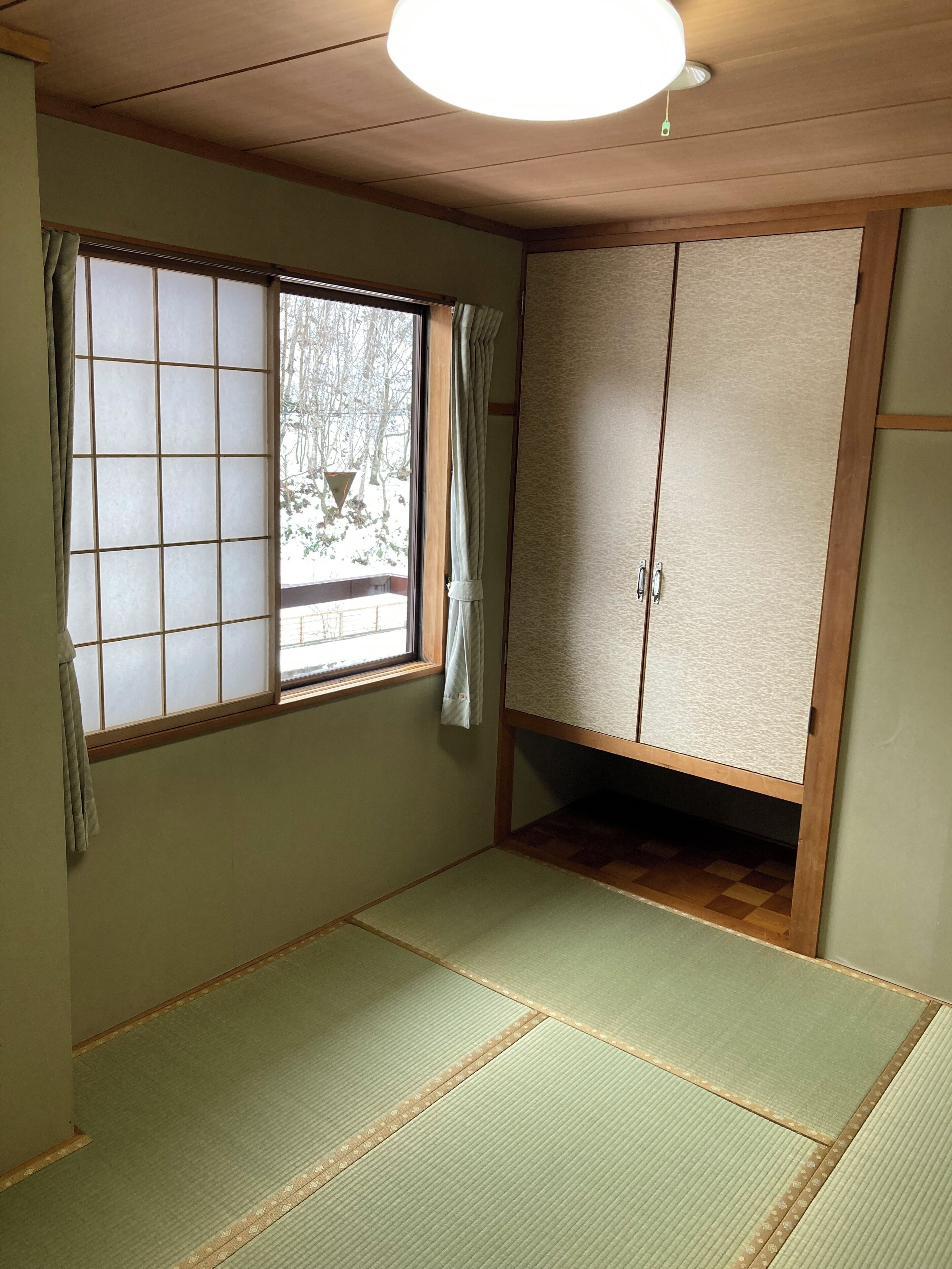 Una habitación con suelo de tatami, un panel corredero shoji, un armario y un ventilador de techo.