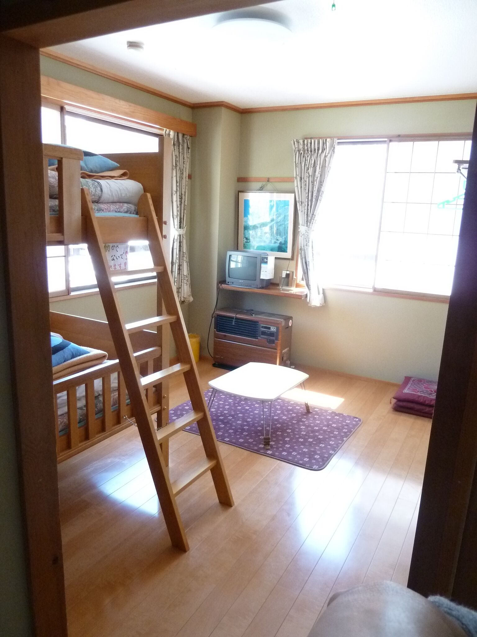 Una habitación con literas, un escritorio con computadora, una ventana con cortinas y piso de madera.