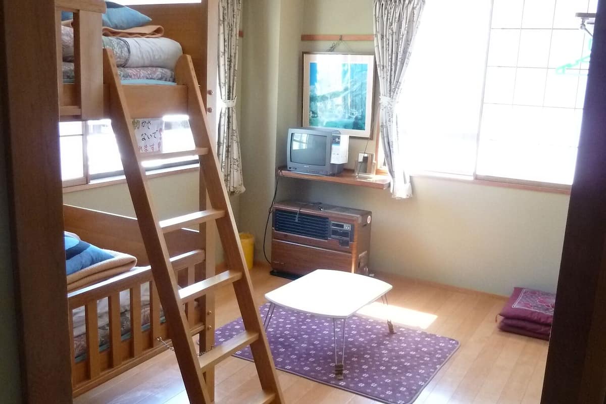 A room with bunk beds, a desk with a computer, a window with curtains, and a wooden floor.