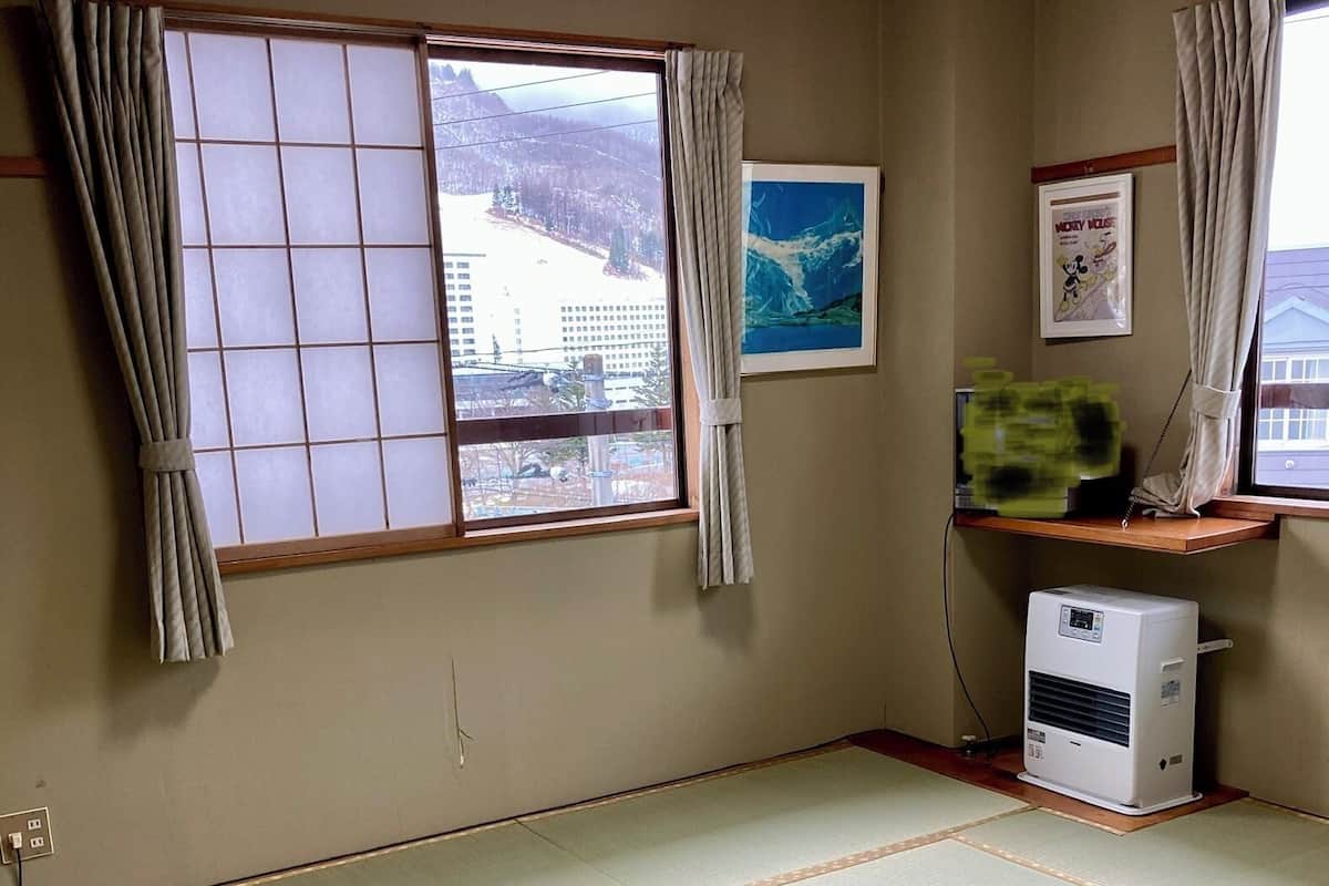 A room with tatami mats, a heater, a window with curtains, and a framed picture.