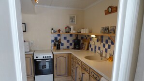Een kleine keuken met een kookplaat, oven, spoelbak en een betegelde spatwand.