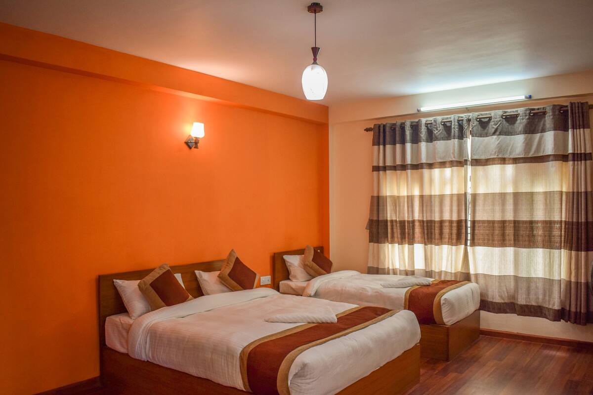 A hotel room with two beds, a wooden headboard, a wall-mounted lamp, and striped curtains.