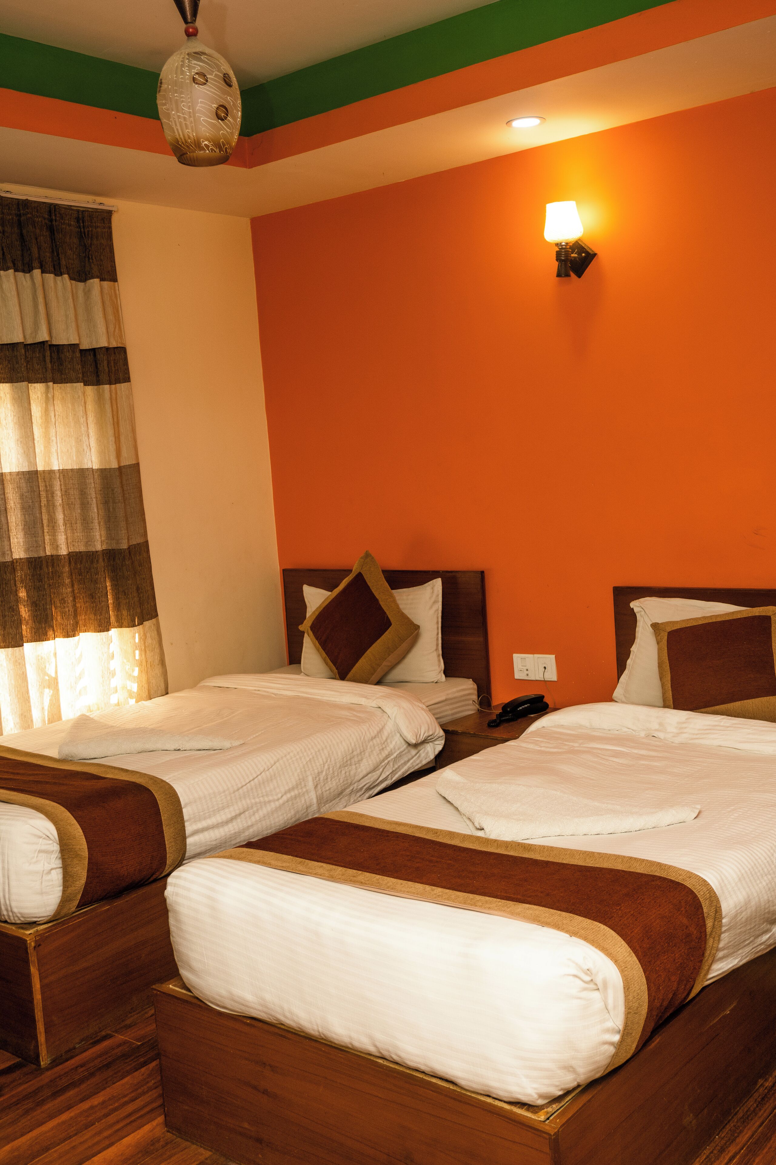 A hotel room with two wooden beds, a striped curtain, and a wall-mounted lamp.