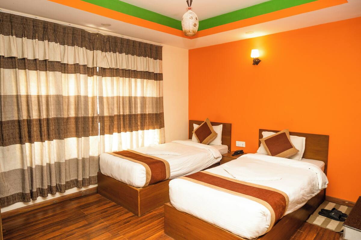 A hotel room with two beds, wooden flooring, striped curtains, and an orange wall.