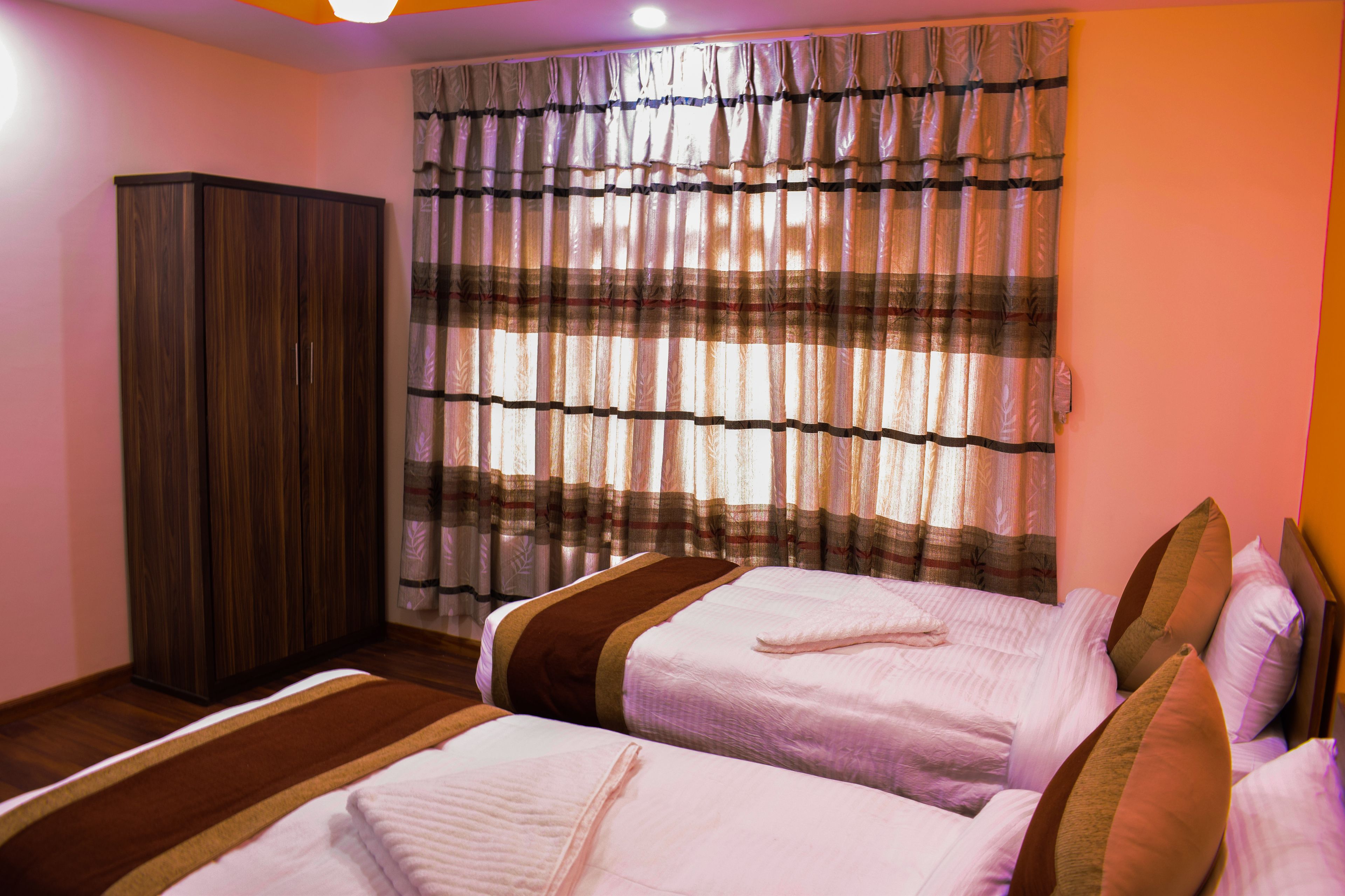 A hotel room with two beds, a wardrobe, and a window with curtains.