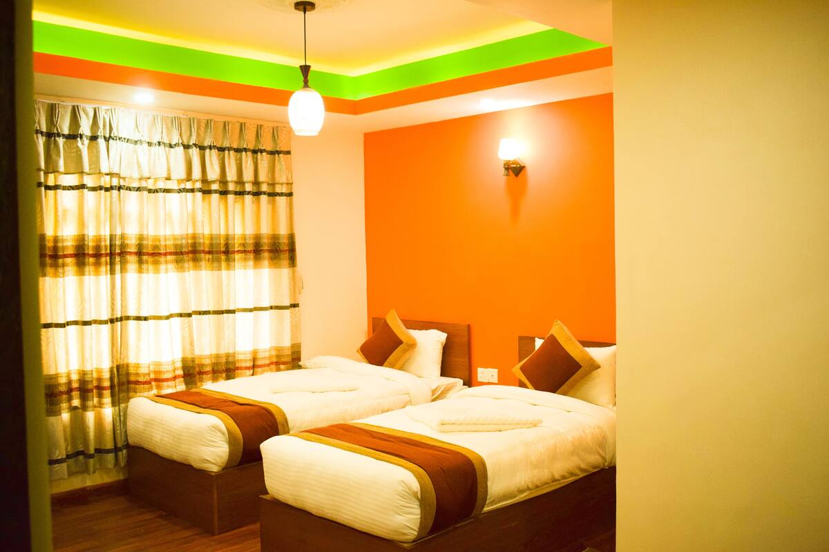 A hotel room with two beds, a window with curtains, and a wall with a light switch.
