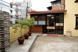 Un edificio con puerta de vidrio, plantas en macetas y felpudo rojo en la entrada.